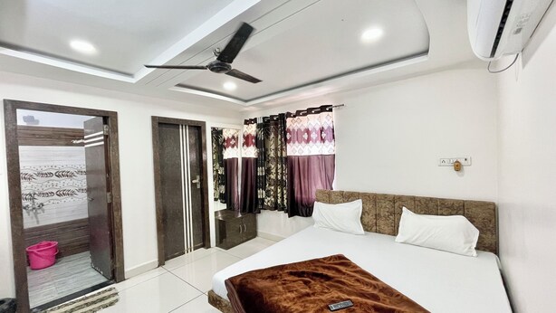 A modern hotel room with a large bed, a ceiling fan, and a window with curtains. - Hotel S M INN near Temple & Main Places (Ujjain)