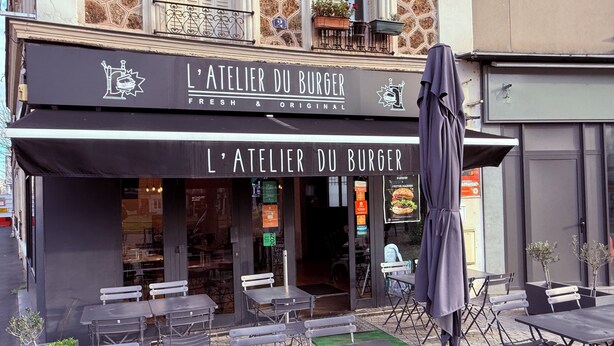 Ein Sitzbereich im Freien mit Tischen und Stühlen vor einem Restaurant namens L'Atelier Du Burger.