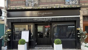 Eine Schaufensteransicht mit dem Schild "LES GOURMANDS" und "L'ORFERVERIE DU BURGER", das ein Restaurant kennzeichnet.
