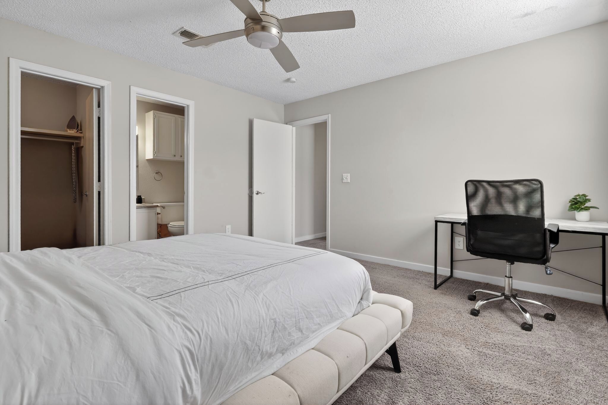A bedroom with a bed, a desk, a chair, and a ceiling fan.