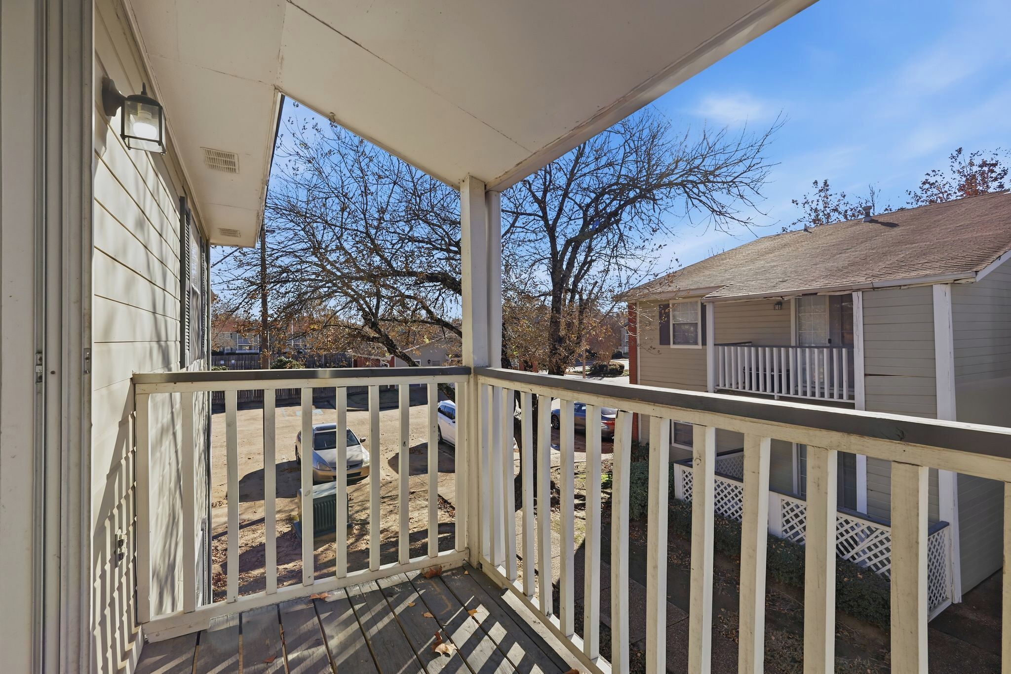A covered porch with a white railing, a small shed in the background, and a clear sky.