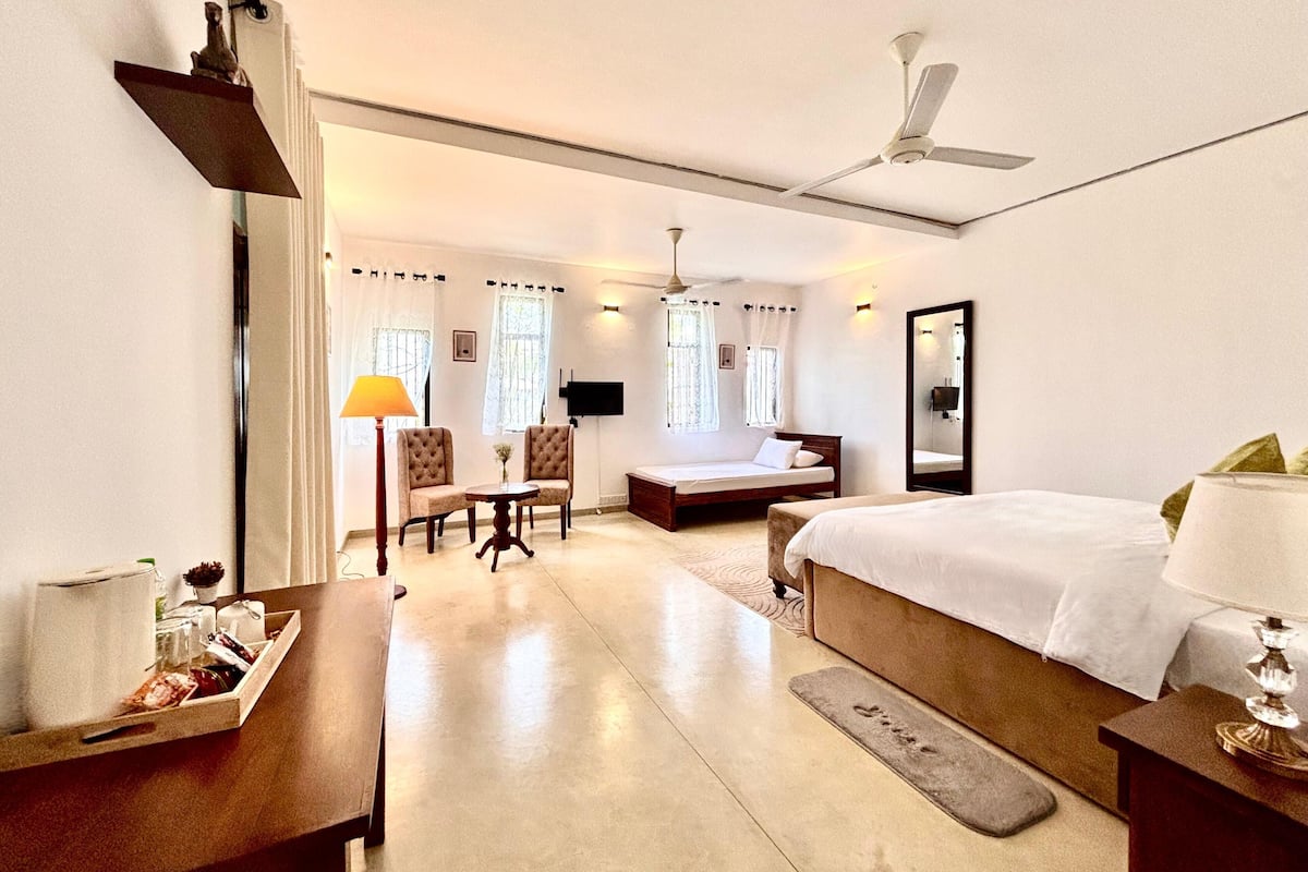 A hotel room with a bed, a desk, a chair, a small table, and a TV.
