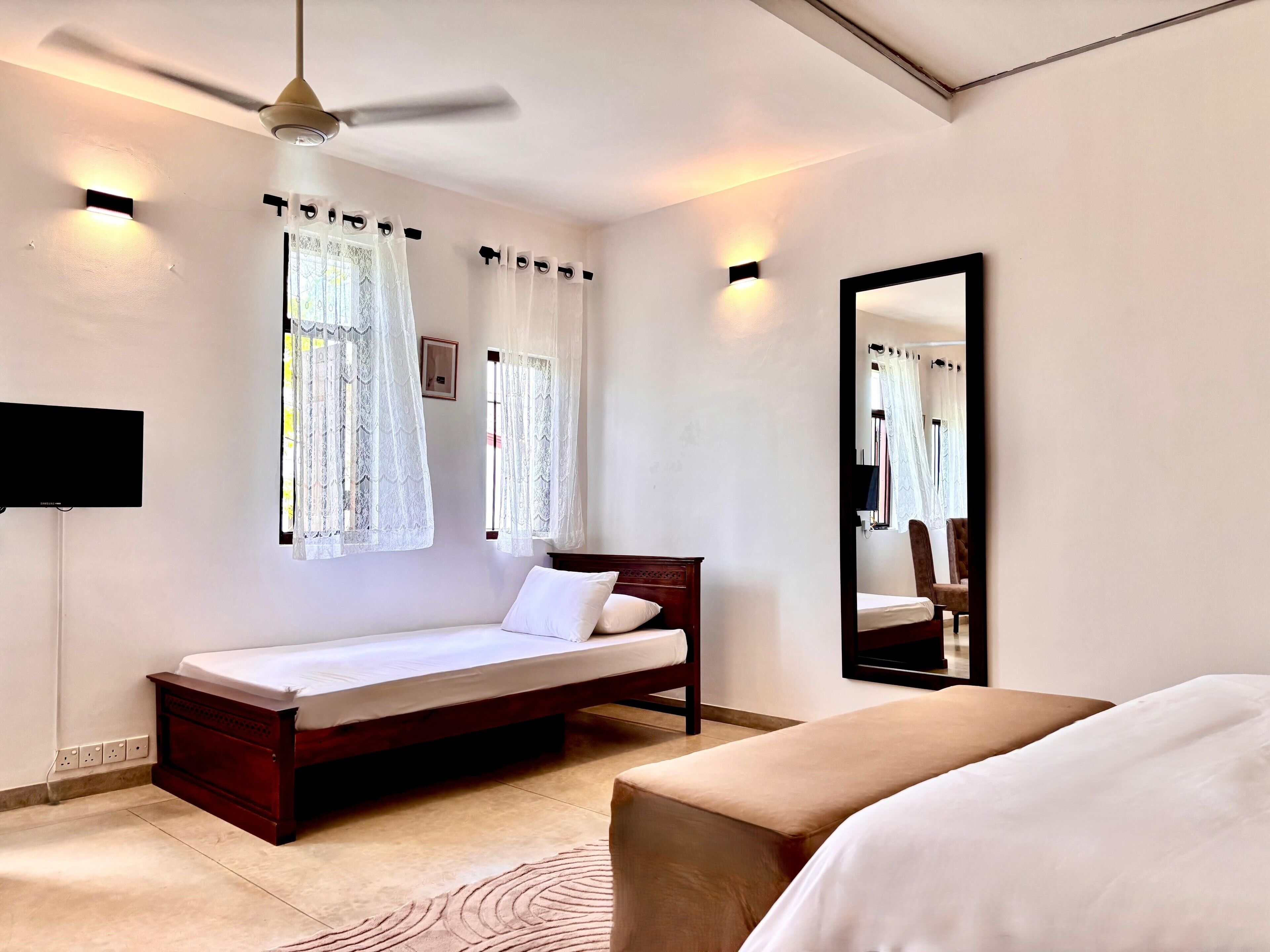 A bedroom with a bed, a bedside table, a mirror, and a ceiling fan.