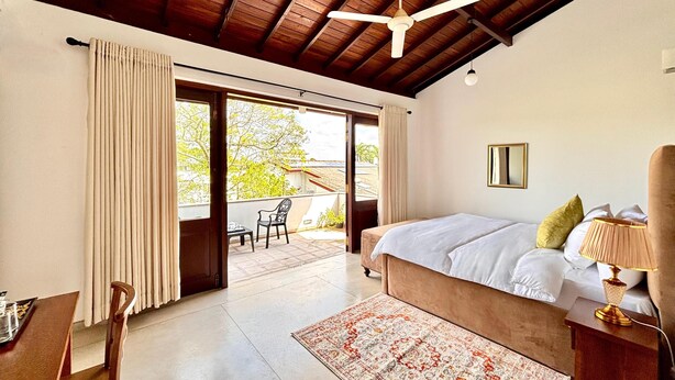 Ein Schlafzimmer mit einem großen Bett, einem Deckenventilator, Blick auf eine Außenpatio und einem Essbereich mit Tisch und Stühlen.