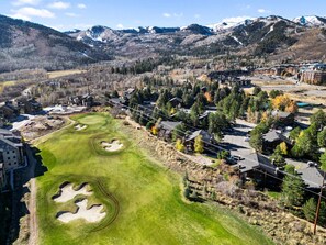 Ein Golfplatz mit Bunkern, umgeben von Wohngebäuden und einer Bergkulisse.
