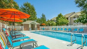 A pool area with blue lounge chairs and orange umbrellas, surrounded by a white fence and trees. - Modern Comfort w/ Balcony, Kitchen & WiFi (Birmingham)