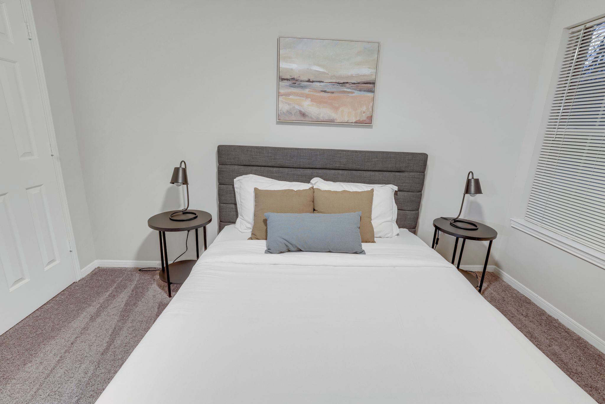 Un dormitorio ordenado con cama, dos mesitas de noche, cabecera y una obra de arte colgada en la pared.