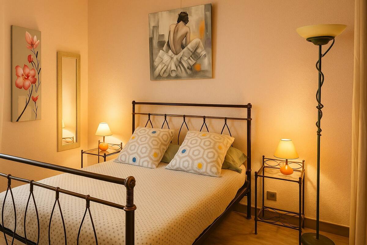 A bedroom with a bed, two bedside tables, a floor lamp, a mirror, and artwork on the walls.