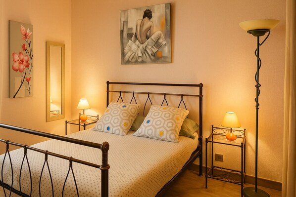 A bedroom with a bed, two bedside tables, a floor lamp, a mirror, and artwork on the walls. - HOTEL PERPIGNAN CENTRE (Perpignan)