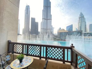 A balcony with a view of the Burj Khalifa and other skyscrapers, a pool with water fountains, and a table with a potted plant. - Durrani Homes - Heaven on Earth (Dubai)
