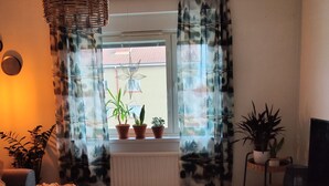 En hyggelig stue med en sofa, et sofabord og et TV-møbel. Der er plantede planter på vindueskarmen og en hængende lampe.