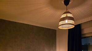 Et soveværelse med en seng, to sengeborde med lamper, en hængende loftlampe, et vindue med gardiner og et trægulv.