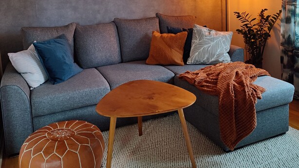 En moderne stue med en grå sofa, et træbord og en pyntepude med mønster.