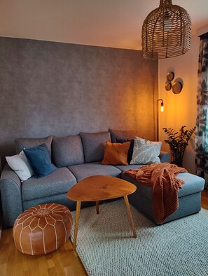 Una sala moderna con un sofá gris, una mesa de centro de madera y un otomano estampado.
