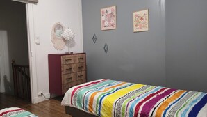 A bedroom with a wooden wardrobe, a colorful striped bedspread, and two framed floral artworks on the wall. - House with a garden in Le Havre, quiet location, near the tram, sleeps 2 to 6 people.  (Le Havre)