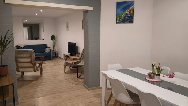 A modern living room with a blue sofa, a TV, and a dining area with a table and chairs. - House with a garden in Le Havre, quiet location, near the tram, sleeps 2 to 6 people.  (Le Havre)