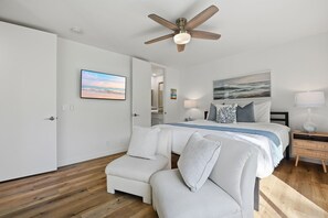 A bedroom with a bed, a chair, a nightstand, a lamp, a ceiling fan, and artwork on the walls. - New Listing: Beautiful Interior with Two Balconies – North Coast Village G101 (Oceanside)