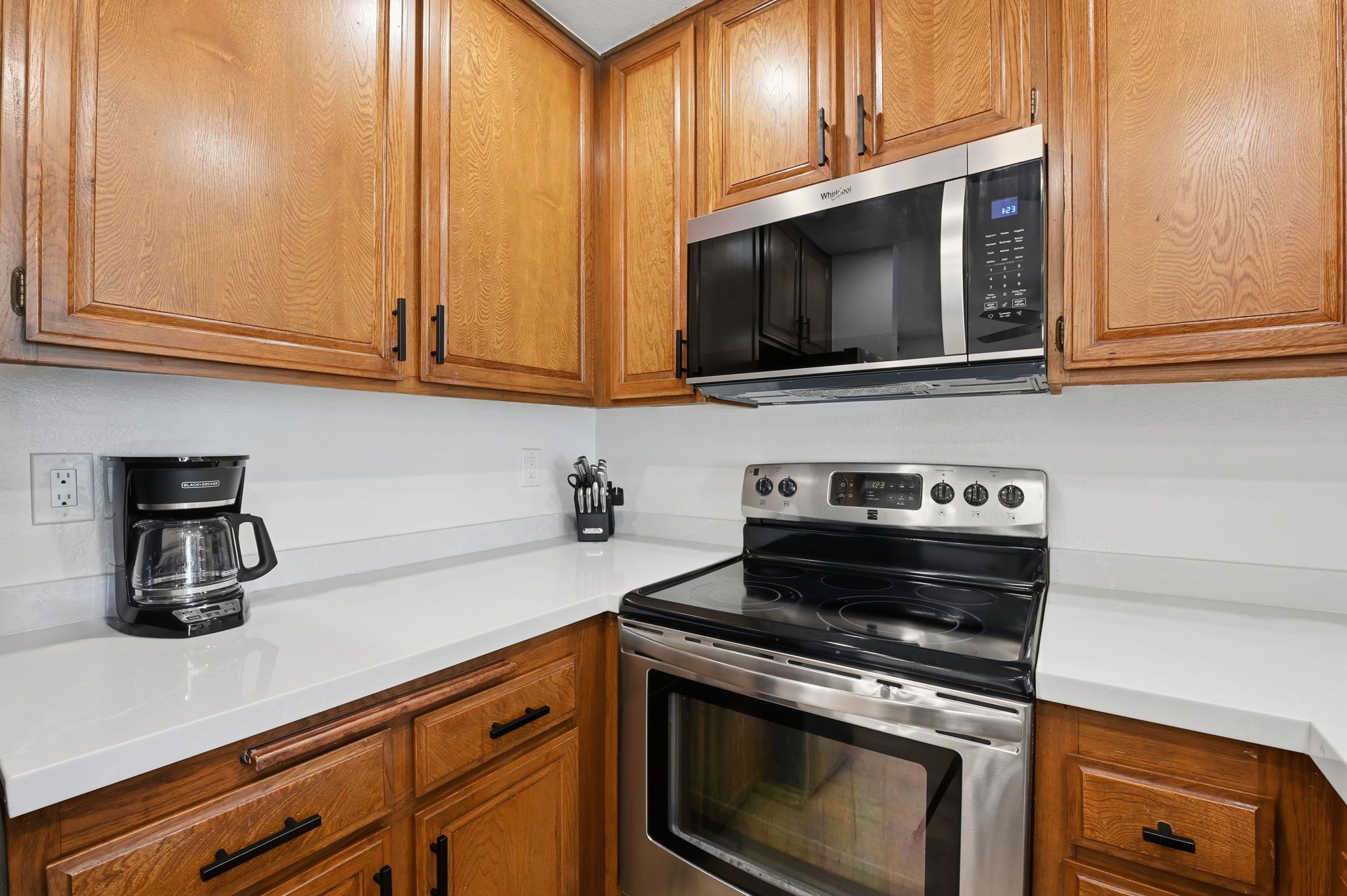 A kitchen with wooden cabinets, a microwave, a stove, and a coffee maker.