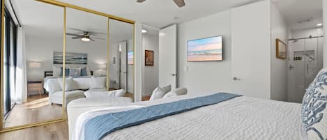 A bedroom with a large bed, a ceiling fan, a mirror, and a view of the bathroom.