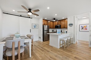 A modern kitchen with wooden cabinets, a stainless steel refrigerator, and a bar area with stools. - New Listing: Beautiful Interior with Two Balconies – North Coast Village G101 (Oceanside)