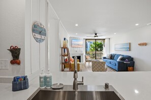 A modern kitchen with a stainless steel sink, a wooden ladder, and a blue sofa in the living area. - New Listing: Beautiful Interior with Two Balconies – North Coast Village G101 (Oceanside)