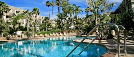 A resort pool with clear blue water, surrounded by palm trees and lounge chairs.