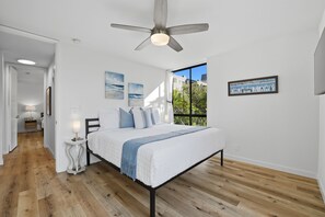 Ein Schlafzimmer mit Bett, Deckenventilator, Fenster mit Blick und Kunstwerken an den Wänden.