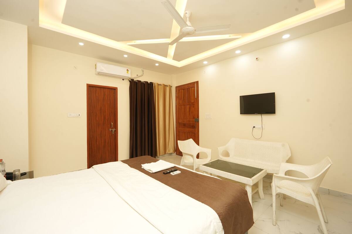 A hotel room with a bed, a desk, two chairs, a television, and a ceiling fan.