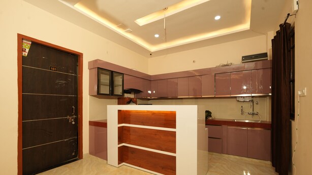 A modern kitchen with a dark wooden door, a built-in white counter, and purple cabinets. - Hotel Rahul inn  (Lucknow)