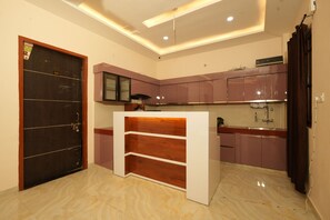 A modern kitchen with a dark wooden door, a built-in white counter, and purple cabinets. - Hotel Rahul inn  (Lucknow)