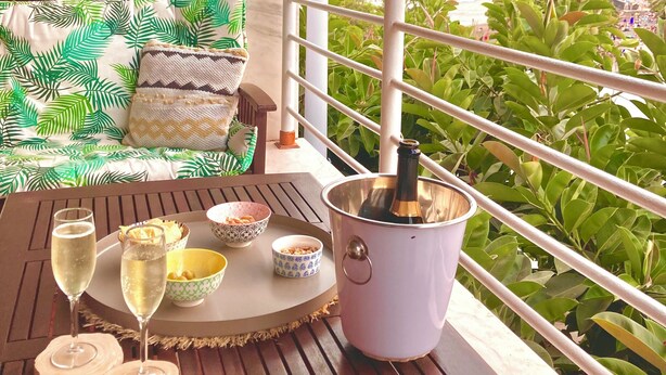 En balkon med et bord dækket til et drikkespil, en champagneflaske og udsigt til frodig vegetation og et fjerntliggende bjerg.