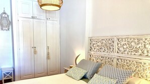 Et pænt opredt soveværelse med seng, mønstrede puder, et dekorativt sengegærde, et garderobeskab og en hængende lampe.