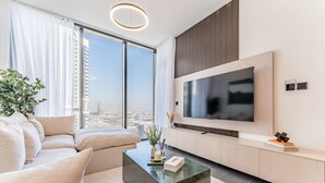 A modern living room with a large flat-screen TV, a sofa, a coffee table, and a view of the city through large windows. - Prime 1BR, Few minutes Drive to Burj Khalifa and Dubai Mall - Sobha Hartland The Crest Tower C  by Deluxe Holiday Homes (Dubai)