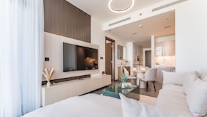 A modern hotel room with a large bed, a flat-screen TV mounted on the wall, a dining area with a table and chairs, and a kitchen area with a sink and cabinets. - Prime 1BR, Few minutes Drive to Burj Khalifa and Dubai Mall - Sobha Hartland The Crest Tower C  by Deluxe Holiday Homes (Dubai)