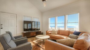 Un salón amplio con un televisor grande, asientos cómodos y vista al océano.