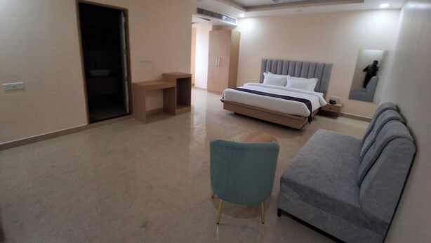 Una habitación de hotel con una cama, un sofá gris, una mesita y una silla.