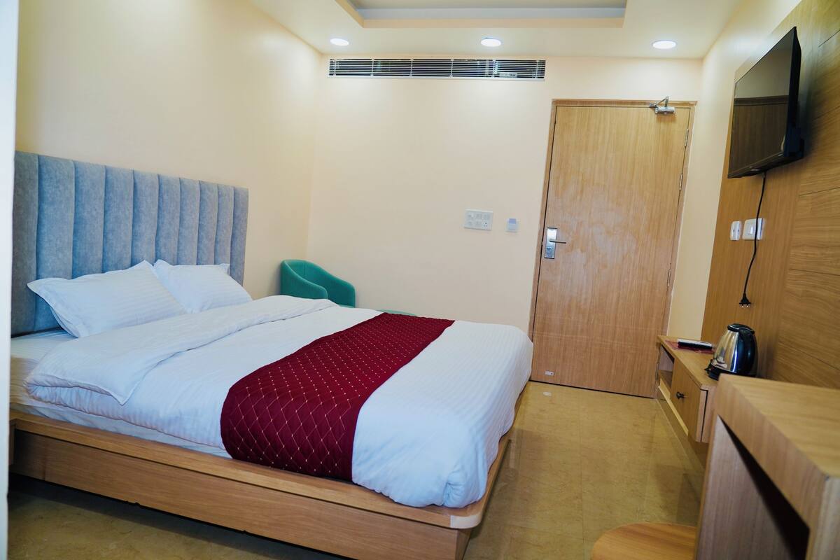 A single bed with a headboard, a wooden nightstand, a television mounted on the wall, and a door with a handle.