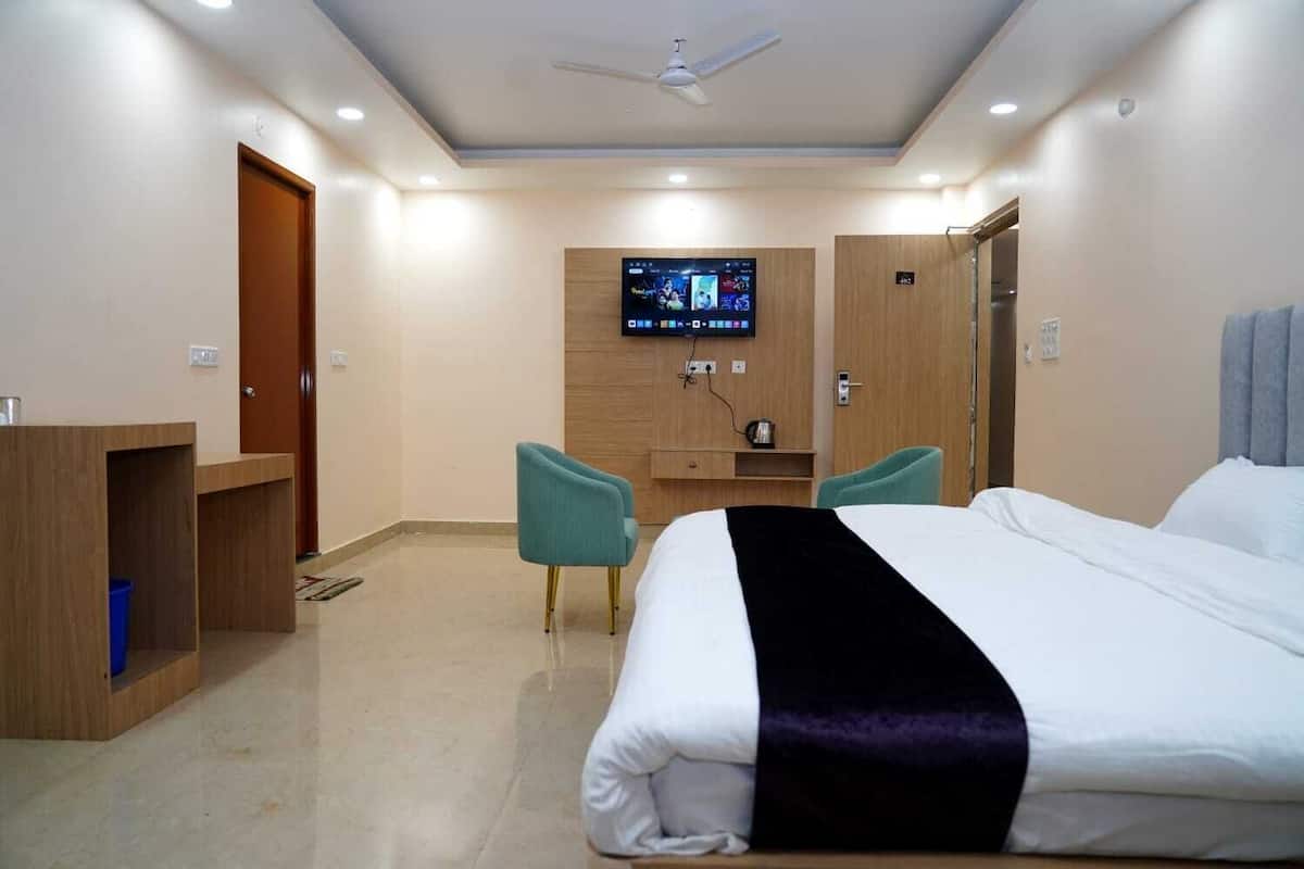 A hotel room with a bed, a desk, two chairs, a television, and a ceiling fan.