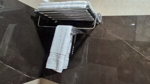 Un baño con un perchero que sostiene varias toallas blancas y una toalla gris. El piso está cubierto de baldosas con un diseño de mármol oscuro.
