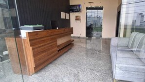 Un área de recepción con un escritorio de madera, un sofá gris y un televisor montado en la pared.