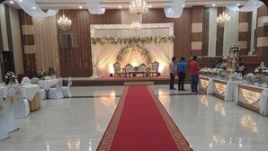 Un salón de banquetes con pasillo de alfombra roja, mesas con manteles blancos y candelabros.