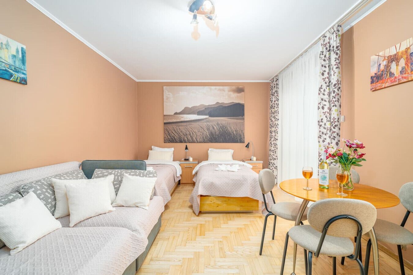 Une pièce confortable avec un lit, un canapé et une table à manger avec des chaises. Il y a un tableau au mur et une fenêtre avec des rideaux.