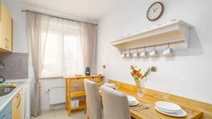 Cocina compacta con zona de comedor, que incluye una mesa de madera dispuesta para dos personas, una cafetera y un reloj en la pared.
