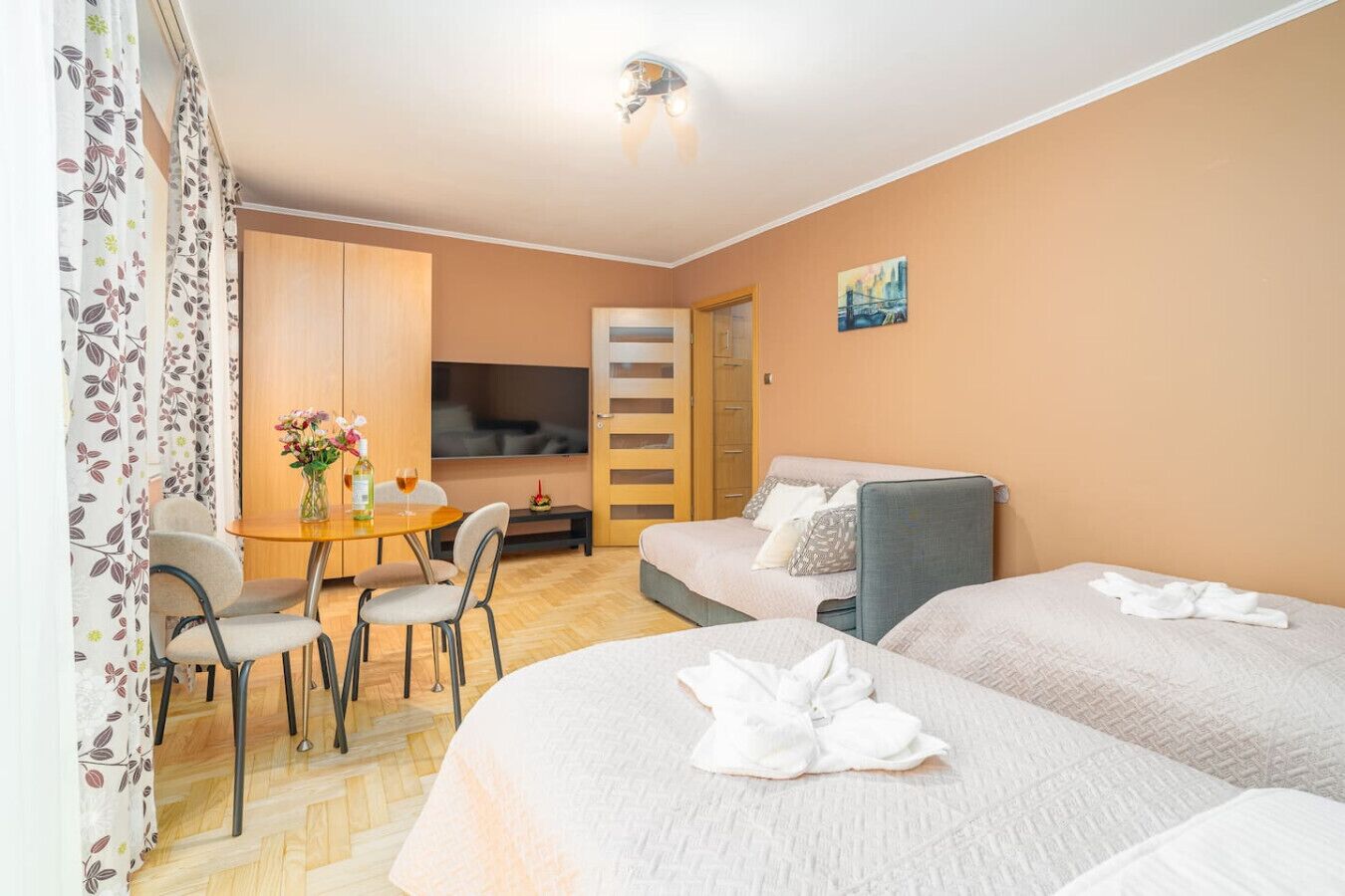 A hotel room with two beds, a dining table with chairs, a TV, and a painting on the wall.