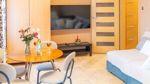 Habitación de hotel con cama, televisión, armario de madera, mesa de comedor con sillas y una pequeña mesa con un florero.