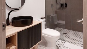 Ein modernes Badezimmer mit einem schwarzen Waschbecken, einer weißen Toilette und einer Duschkabine aus Glas.