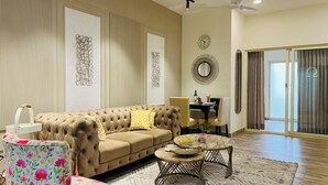 Un salon avec un canapé capitonné, une table basse ronde et un fauteuil à motifs floraux.