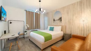 Habitación de hotel con cama, escritorio, silla, sofá y un cuadro en la pared.