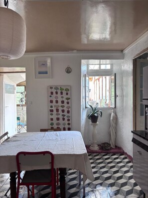 Een kamer met een eettafel, stoelen, een potplant en een betegelde vloer.