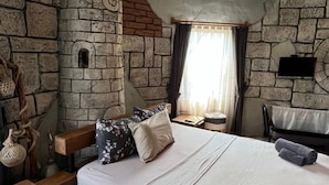 A bedroom with a stone wall, a bed with a wooden headboard, a nightstand, a lamp, and a stone fireplace. - Villas Rustica Fethiye (Fethiye)